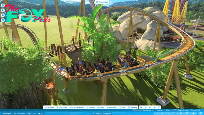 Planet Coaster 2 screenshot showing a rollercoaster cart tearing along a track as it whips up from beneath a wooden bridge surrounded by trees.