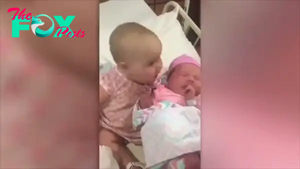 ss.An 8-month-old baby girl tenderly plants a sweet kiss on her newborn cousin in a heartwarming moment captured on camera, leaving onlookers utterly moved